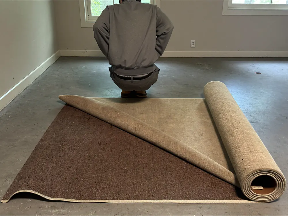Oud kamerbreed tapijt wordt opgerold in een lege kamer met een kale betonvloer