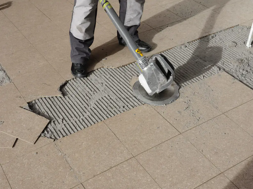 Oude vloertegels worden losgestoken, met de ribbels tegellijm zichtbaar op de dekvloer
